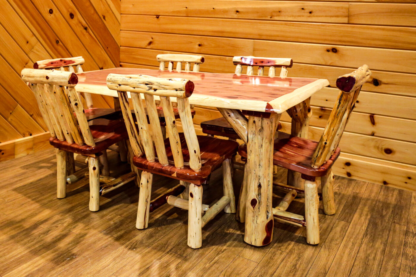 Rustic red cedar dining set with a rectangular table and six matching chairs, featuring natural log frames and polished cedar surfaces.